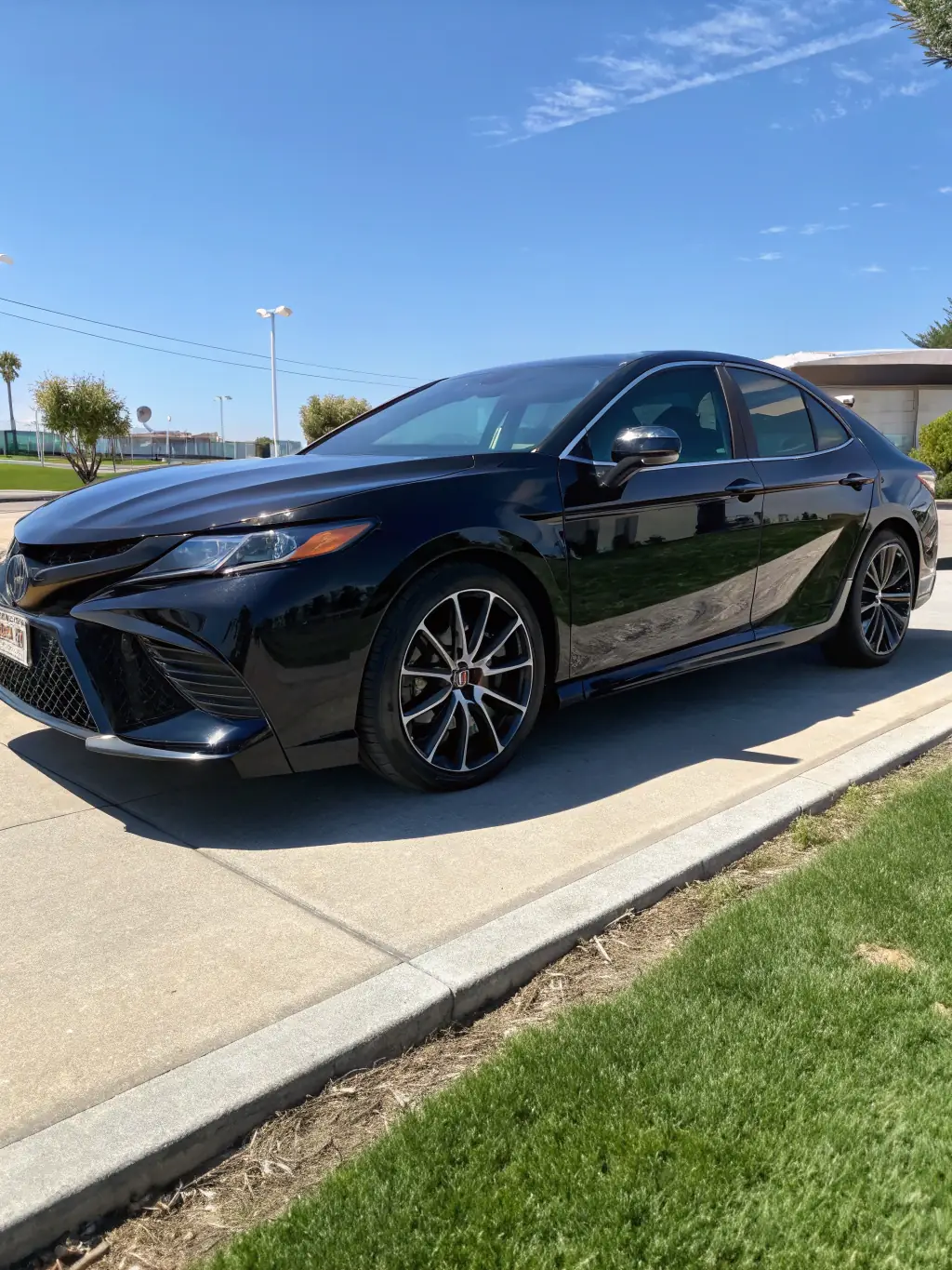 A 2018 Toyota Camry in a vibrant blue color, featuring a sleek aerodynamic design, a bold front grille, and stylish LED headlights. The car has alloy wheels and a smooth body finish, showcasing its modern lines and elegant silhouette.